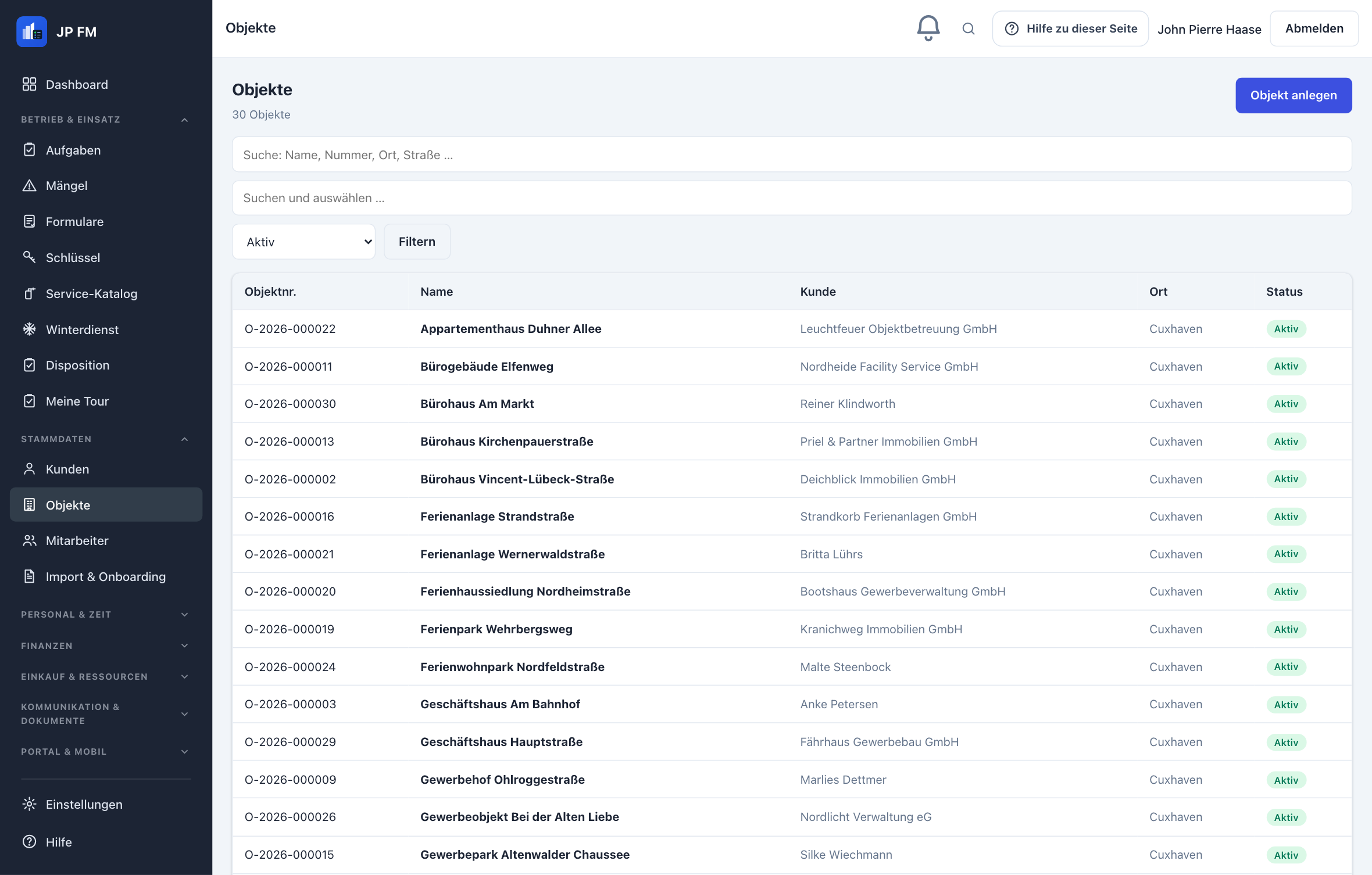 Objektliste in JP FM: links die Modulnavigation, oben die Kopfzeile mit Suche und Hilfe, rechts die Tabelle mit Objektnummer, Bezeichnung, zugeordnetem Kunden, Ort und Status.